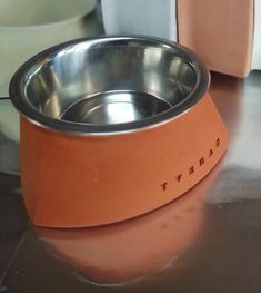 an orange dog bowl sitting on top of a table next to a white and gray dish