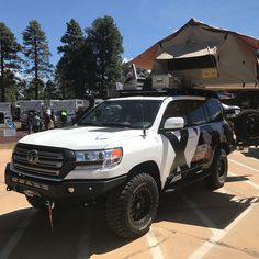 a white truck with black stripes parked in a parking lot next to tents and trees