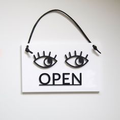 an open sign hanging on the wall with two large eyes and one small eyeball