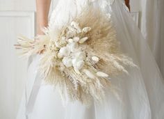 a woman in a white dress holding a bouquet of dried flowers and grasses on her wedding day