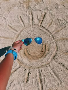 a person wearing sunglasses standing in front of a sundial on the sand with their hands