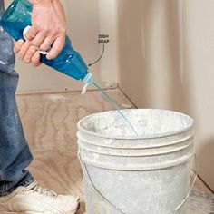 a man is using a blue bottle to fill up a bucket with water on the floor