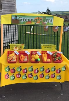 a yellow table topped with lots of fruit and veggies next to a fence