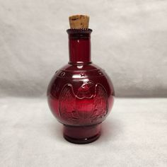 a red glass bottle with a cork in it's top sitting on a white surface