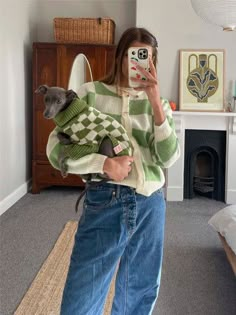 a woman taking a selfie while holding a cat in her arms and wearing a sweater