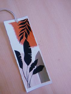 an orange and black tag with leaves on it hanging from a wooden table next to a plant