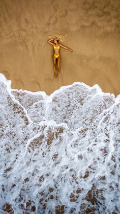 a woman in a yellow bathing suit standing on the beach next to an ocean wave