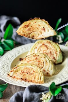 a white plate topped with sliced cabbage on top of a wooden table next to green leaves