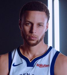 a man with a beard wearing a white and blue basketball uniform looking at the camera