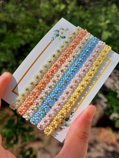 a hand holding several different colored beaded bracelets on top of each other in front of some trees