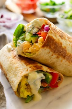 two burritos on a plate with dressing and vegetables