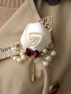 a boutonniere with a white rose and pearls on the lapel pin