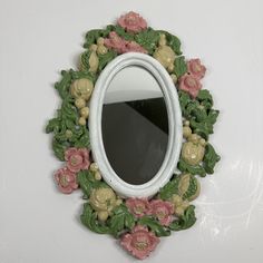 there is a mirror that has flowers on the frame and leaves around it, along with other decorations