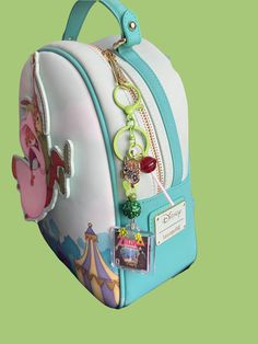 a white and blue suitcase with charms on it's handle, sitting against a green background