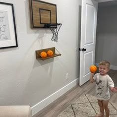 a young boy holding two pumpkins in his hand while standing next to a basketball hoop