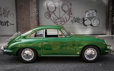 an old green car is parked in front of a building with graffiti on the walls