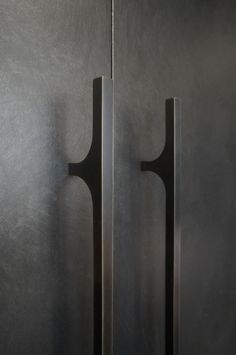 two black doors with handles on them in front of a gray wall and another door handle