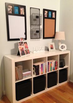 a white book shelf with books and pictures on the wall next to two black bins