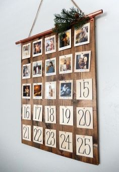 a wooden calendar hanging on the wall with pictures and numbers attached to it, decorated with pine branches