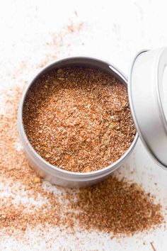 an open can filled with ground spices on top of a white countertop next to a cup of seasoning