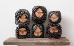 four wooden faces are placed next to each other on top of a wood shelf in front of a white wall