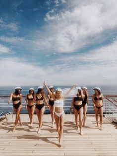 a group of women in bikinis standing on a deck next to the ocean with their arms up