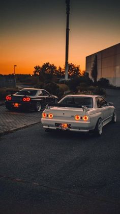 two cars parked next to each other in a parking lot at sunset with the sun setting behind them