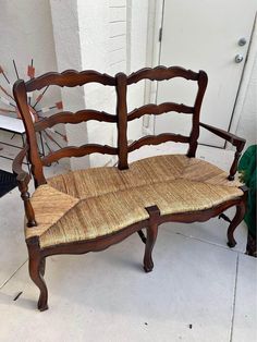 an old wooden bench with wicker seat and back rests on the sidewalk next to a potted plant