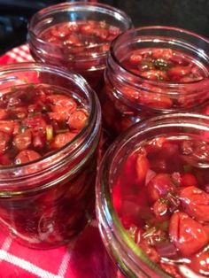 four jars filled with pickled tomatoes on top of a red and white checkered table cloth