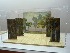 three pieces of art on display in a glass case with wood flooring and trees