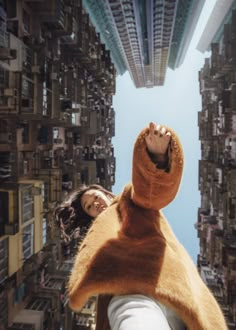 a woman standing in front of a tall building with her hands up to the sky