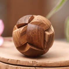 a wooden object sitting on top of a table next to a pink flower in the background