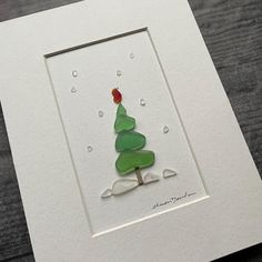 a christmas card with a green tree and a red ball on it's top