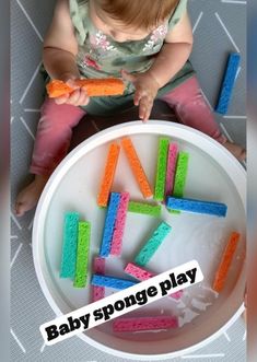 a baby sitting in front of a white bowl filled with colored foams and blocks