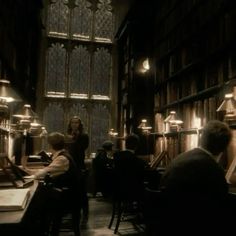 people sitting at tables in a library with bookshelves and lamps on the walls