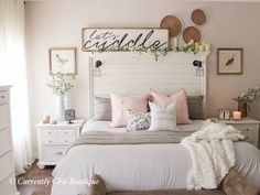 a white bed with pink pillows and blankets on it in a room that has a ceiling fan