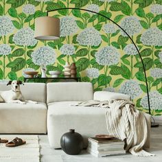 a dog sitting on top of a white couch in front of a green floral wallpaper