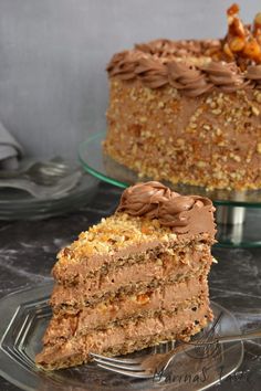 a piece of cake with chocolate frosting and nuts on top sitting on a glass plate