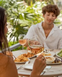 two people sitting at a table with food and wine