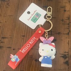 a hello kitty keychain is laying on a wooden table next to a tag