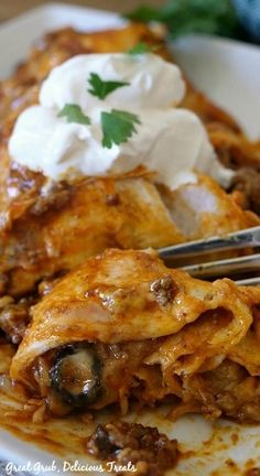 a white plate topped with lasagna covered in sauce and sour cream