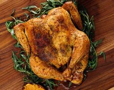 a roasted chicken with herbs and spices on a cutting board next to an orange slice