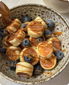 a bowl filled with blueberries and pancakes covered in caramel drizzled