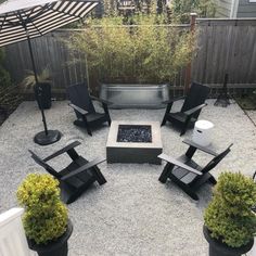 a fire pit surrounded by chairs and umbrellas in a back yard with gravel flooring