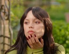 a woman with long black hair is holding her hand to her face and looking at the camera