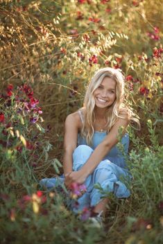 a woman sitting in the middle of a field full of flowers smiling at the camera