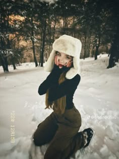 a young woman sitting in the snow with her mouth open and wearing a fur hat