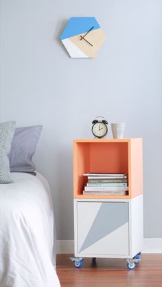 an orange and white nightstand next to a bed with a clock on the wall above it