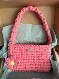 a pink crocheted purse sitting inside of a box on top of a table