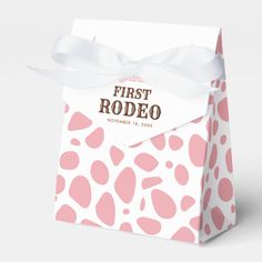 a pink and white polka dot paper bag with a ribbon on the front that says first rodeo